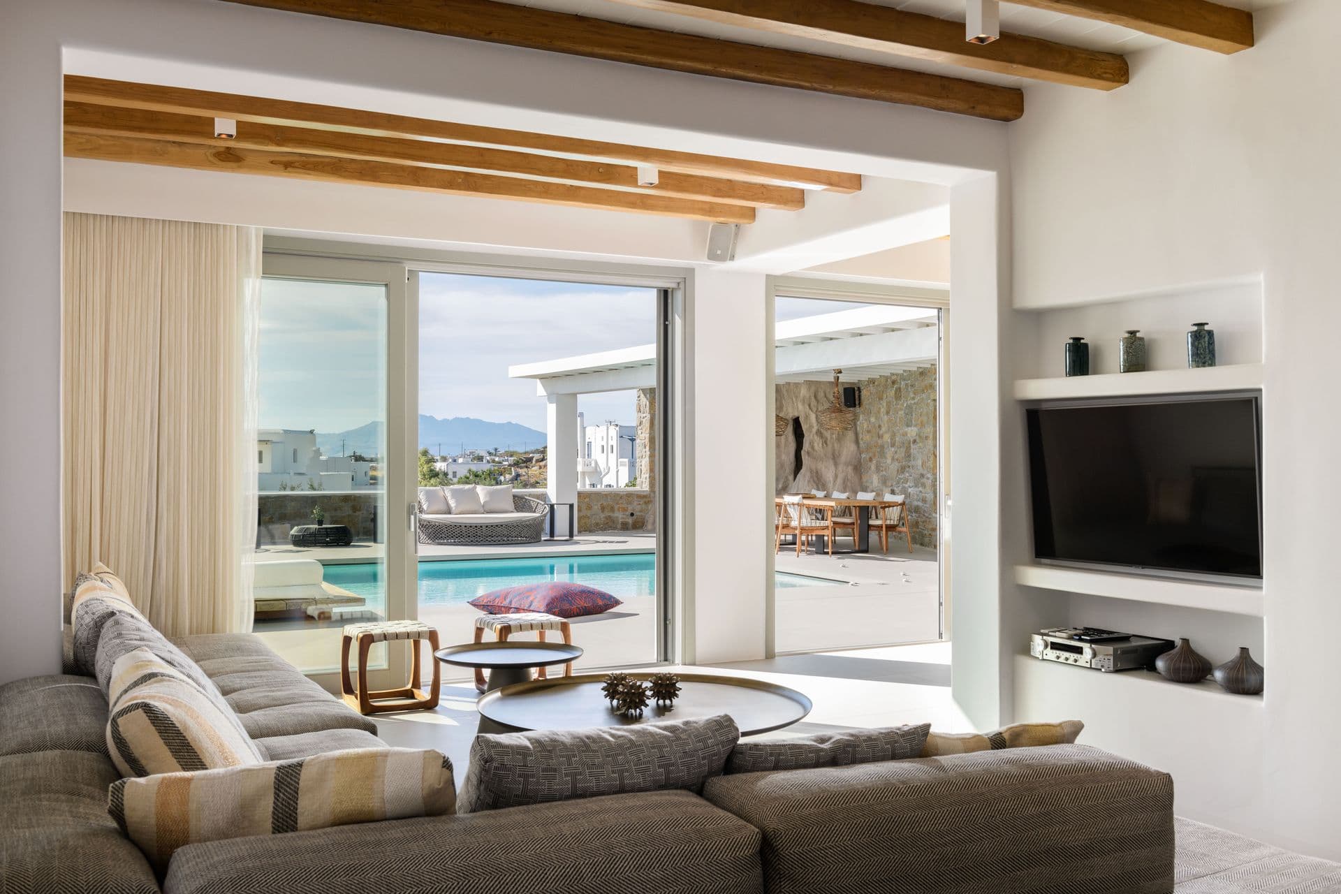 Lounge with a grey sofa and television sliding open to the pool terrace at Cycladic Sunset Stay, Mykonos