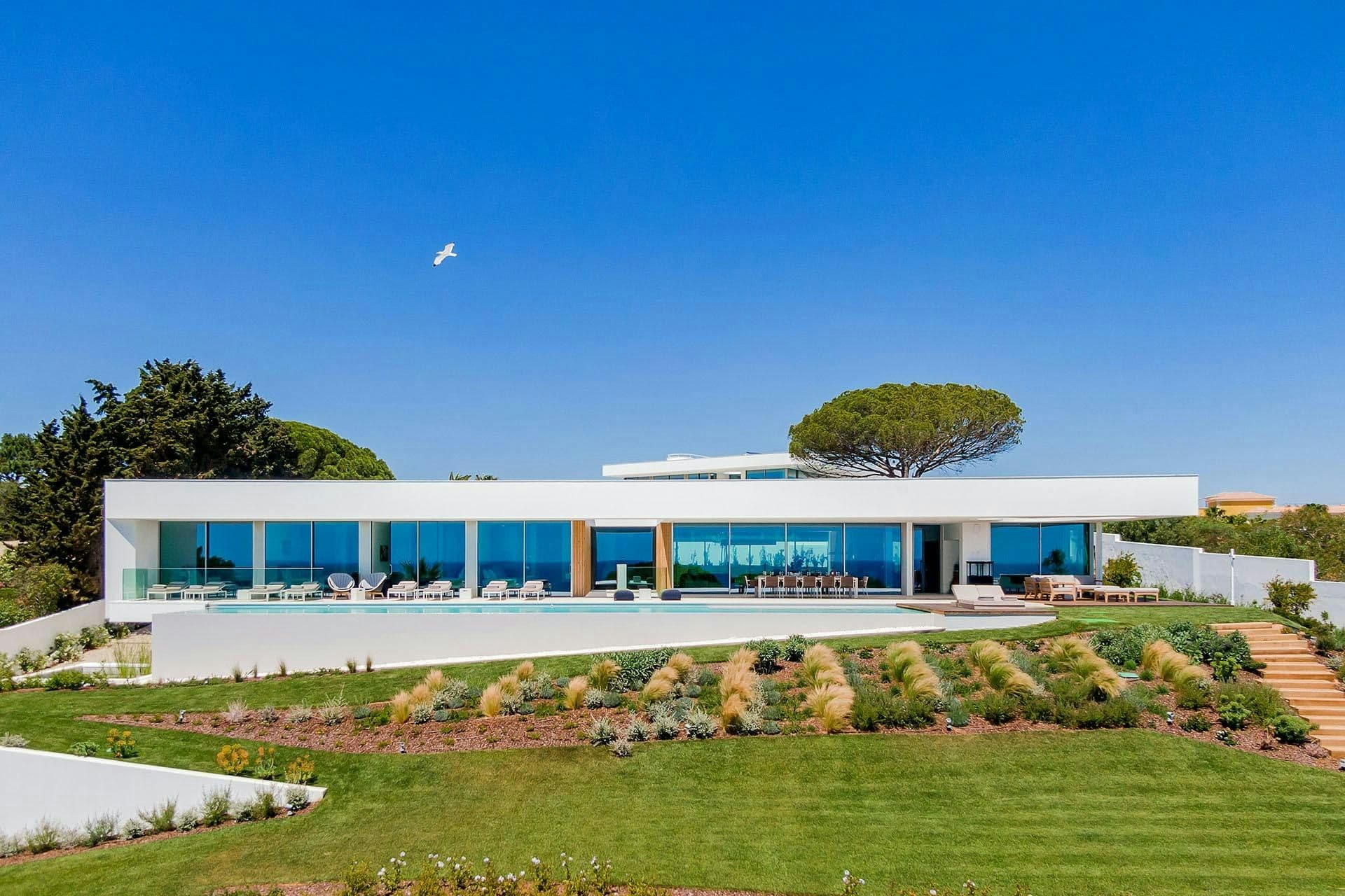 Front elevation of the white modernist villa with its infinity pool and gardens at A Coastal Crown, Lagos