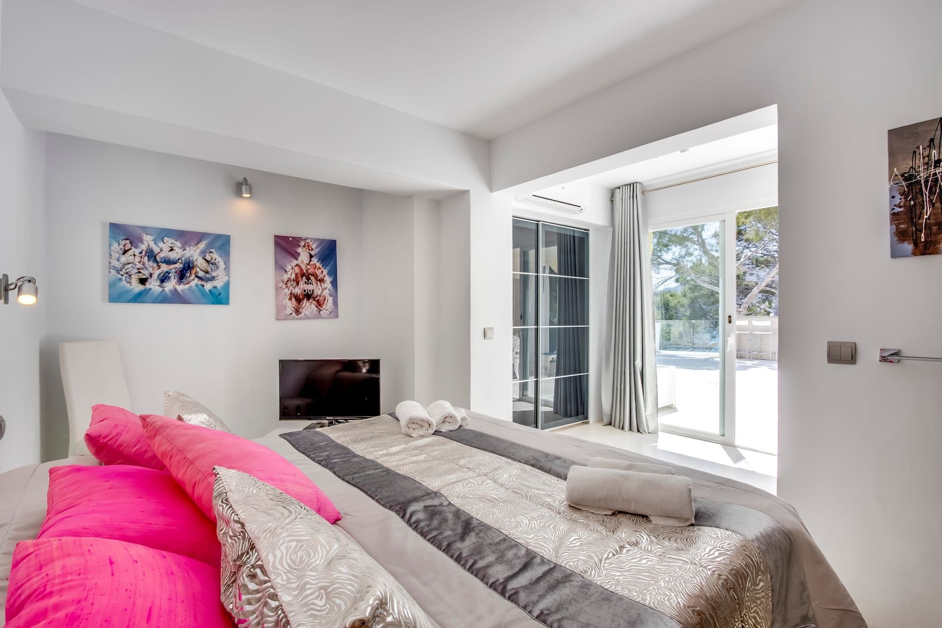 Bedroom with grey bedding, vivid pink accent cushions and terrace access
