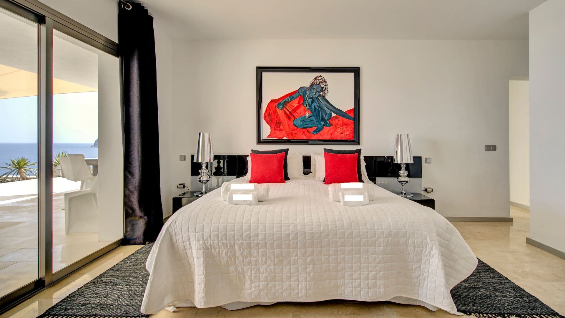 Bedroom with red accent cushions and sliding doors onto a sea view terrace