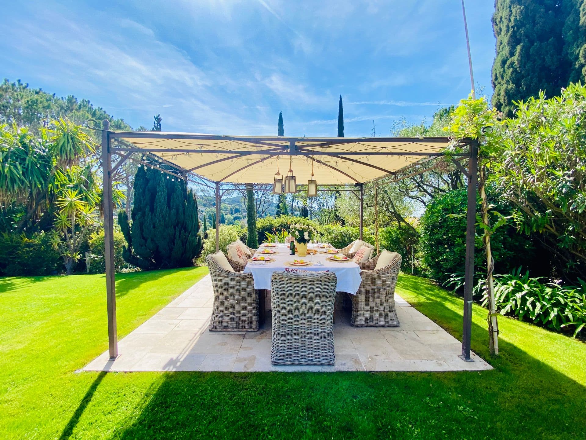 Outdoor dining table for eight under a pergola on the lawn.