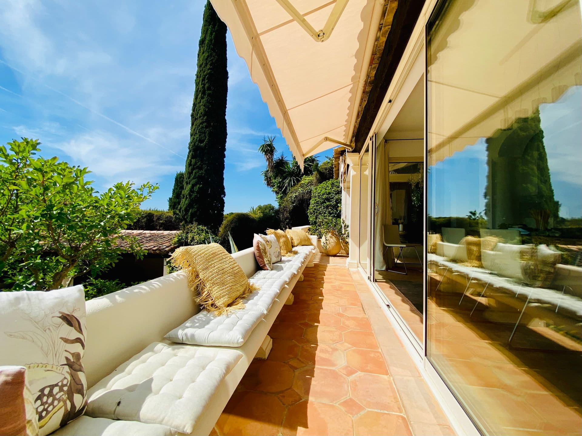 Covered terrace lounge with white daybed seating and garden views.