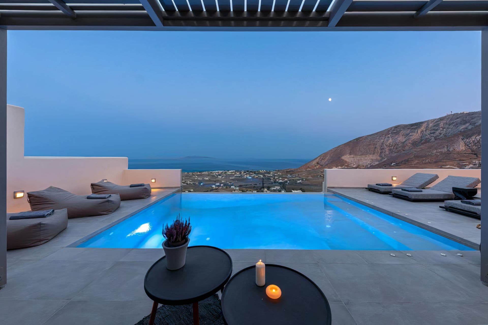 Illuminated infinity pool and lounge seating at twilight overlooking the caldera at Grecian Gazing, Santorini