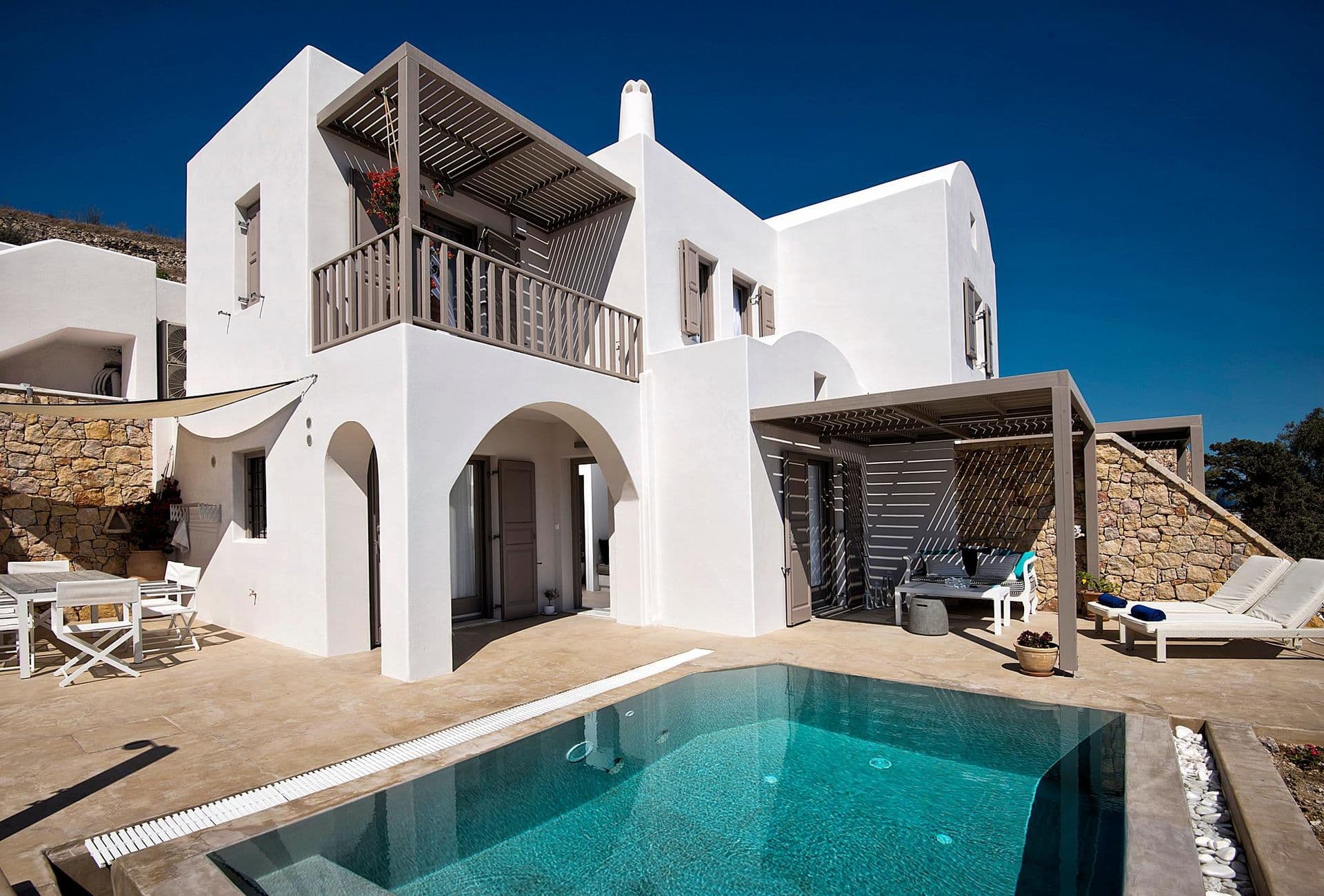 Cycladic whitewashed villa exterior with pool and sun loungers by day at Grecian Gazing