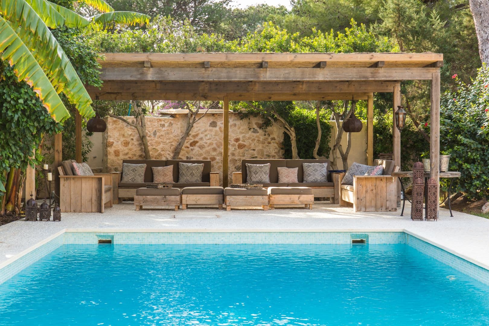 Rectangular swimming pool beside a shaded wooden pergola and sun loungers