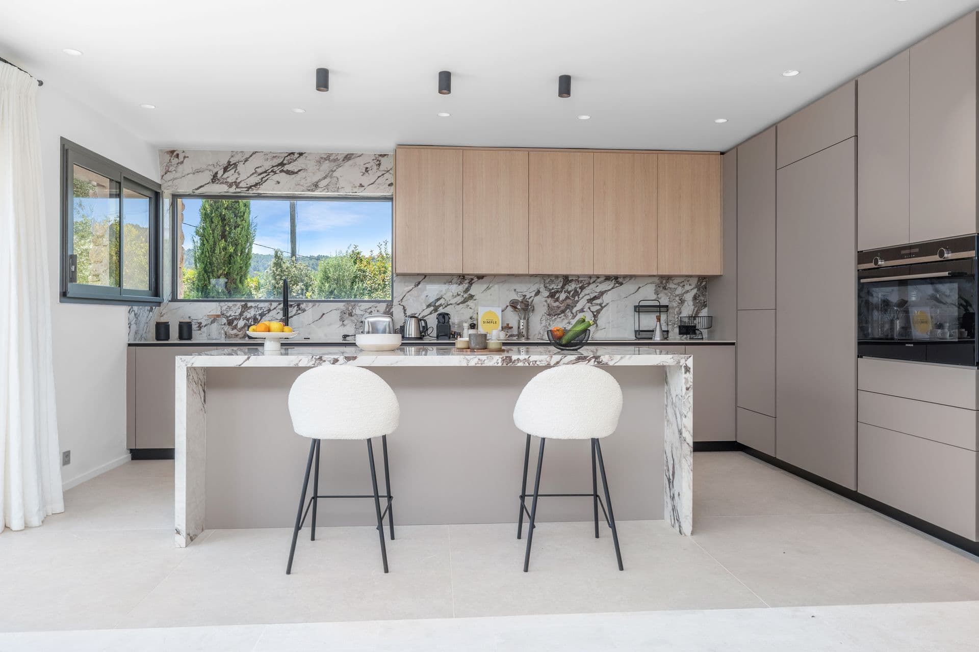 Kitchen with a veined-marble waterfall island and breakfast stools at Alpilles Retreat, Provence