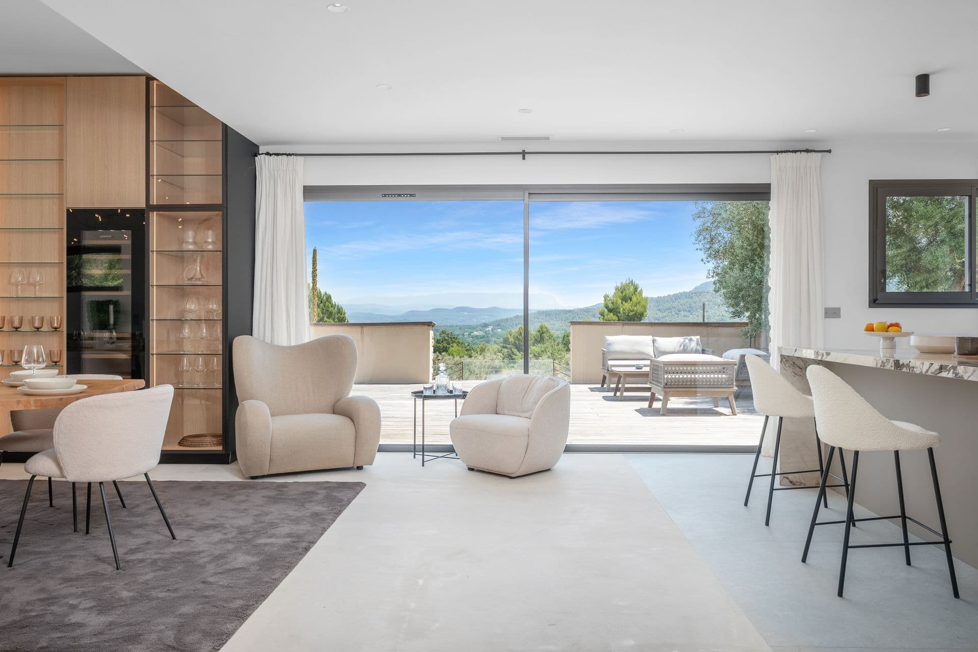 Open-plan living space with armchairs and a breakfast bar opening to the terrace at Alpilles Retreat