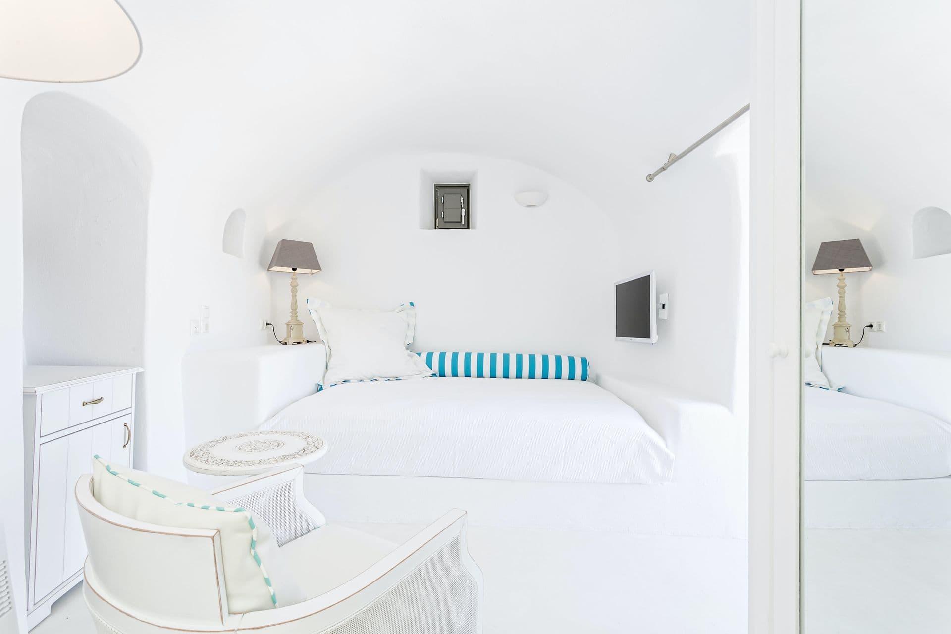White cave bedroom with a blue-striped bolster and armchair at Calypso Dream, Santorini