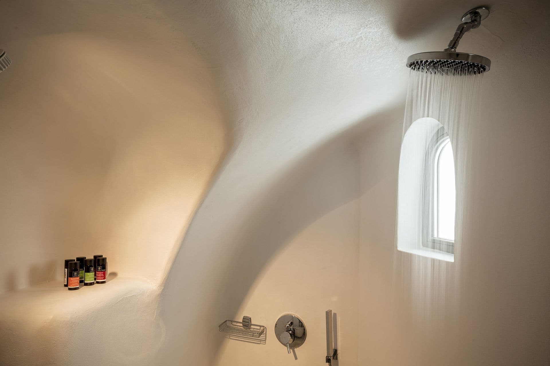 Cave-carved walk-in shower with a small arched window at Calypso Dream, Santorini