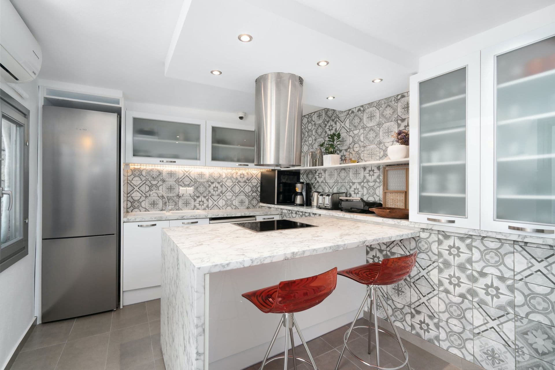 Kitchen with patterned-tile splashback, marble island and red stools at Calypso Dream, Santorini