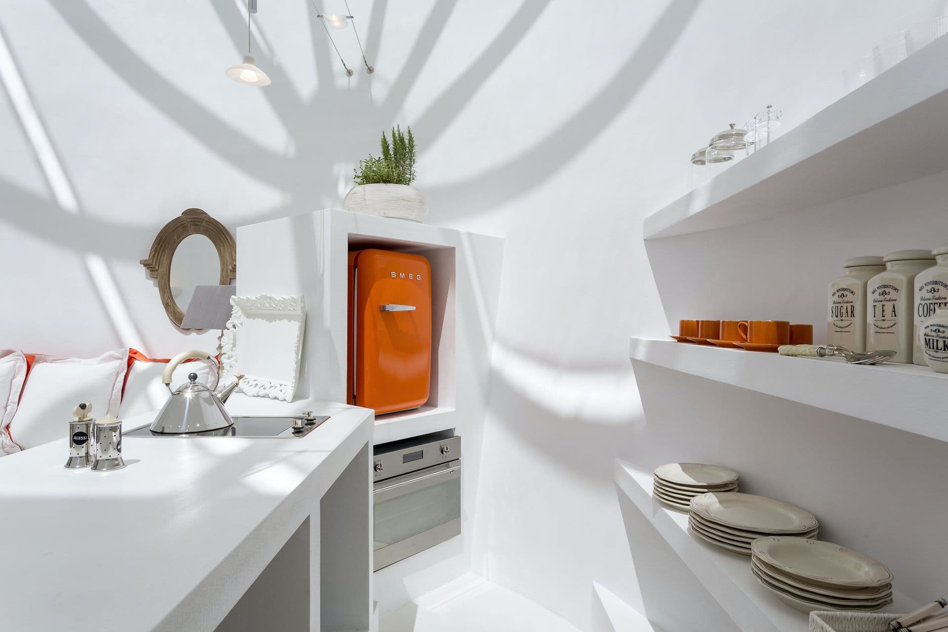 White kitchenette with an orange retro fridge and open shelving at Calypso Dream, Santorini