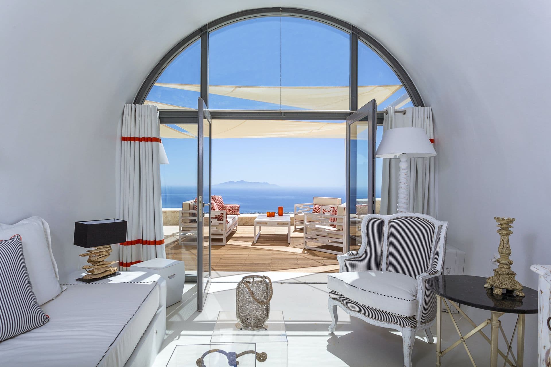 White living room opening through an arched window to a sea-view terrace at Calypso Dream, Santorini