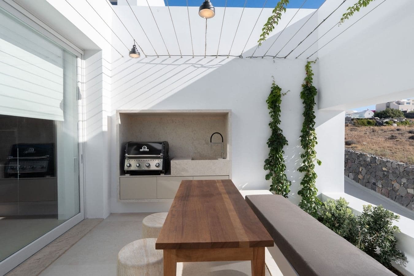 Outdoor kitchen and dining table under a pergola with greenery