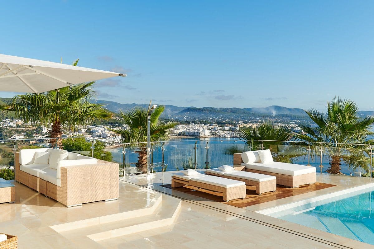 Terrace lounge with white sofas and palms above the bay at Blue Sea Bliss, Ibiza