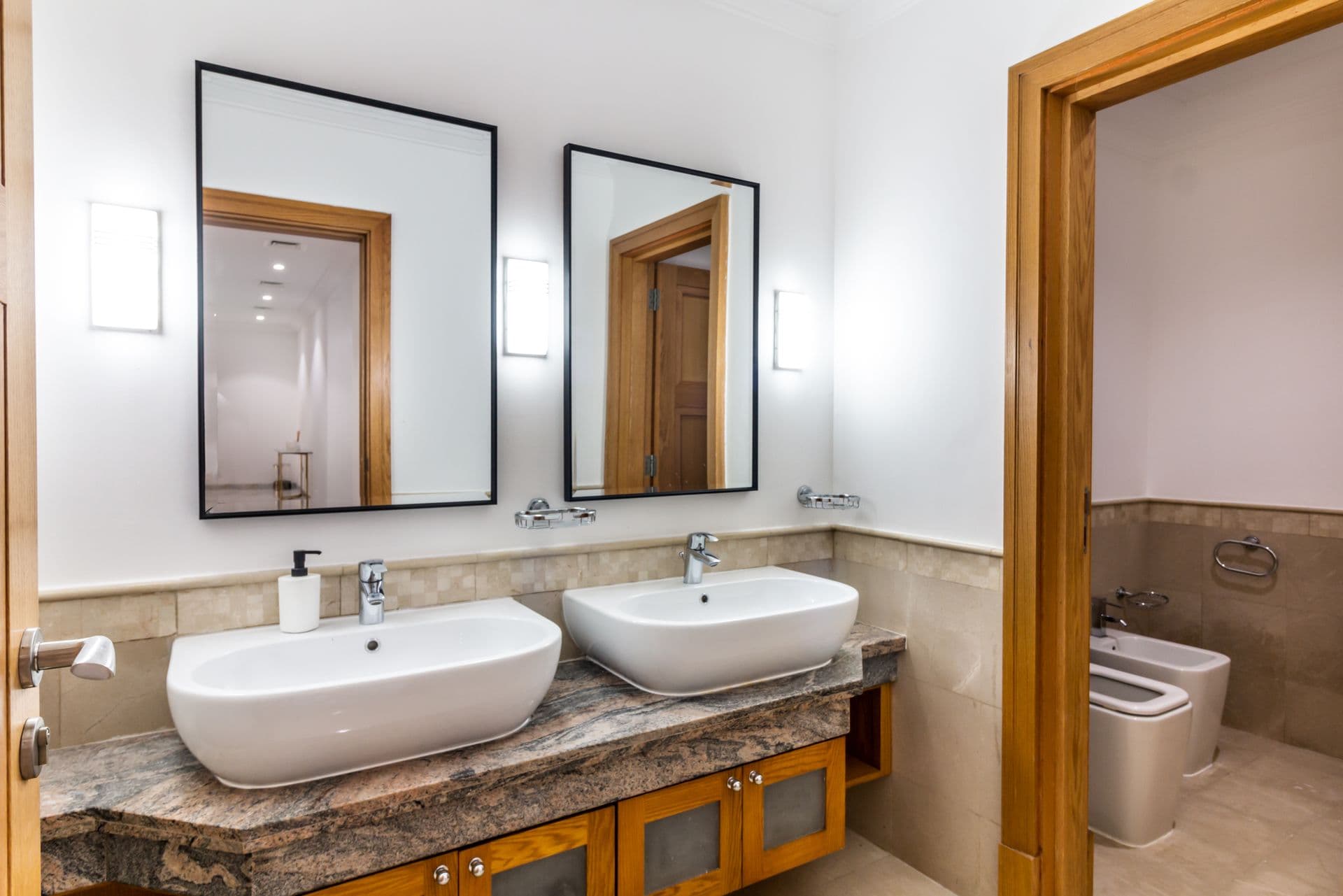 Marble bathroom with double vessel sinks and wood-panelled cabinetry