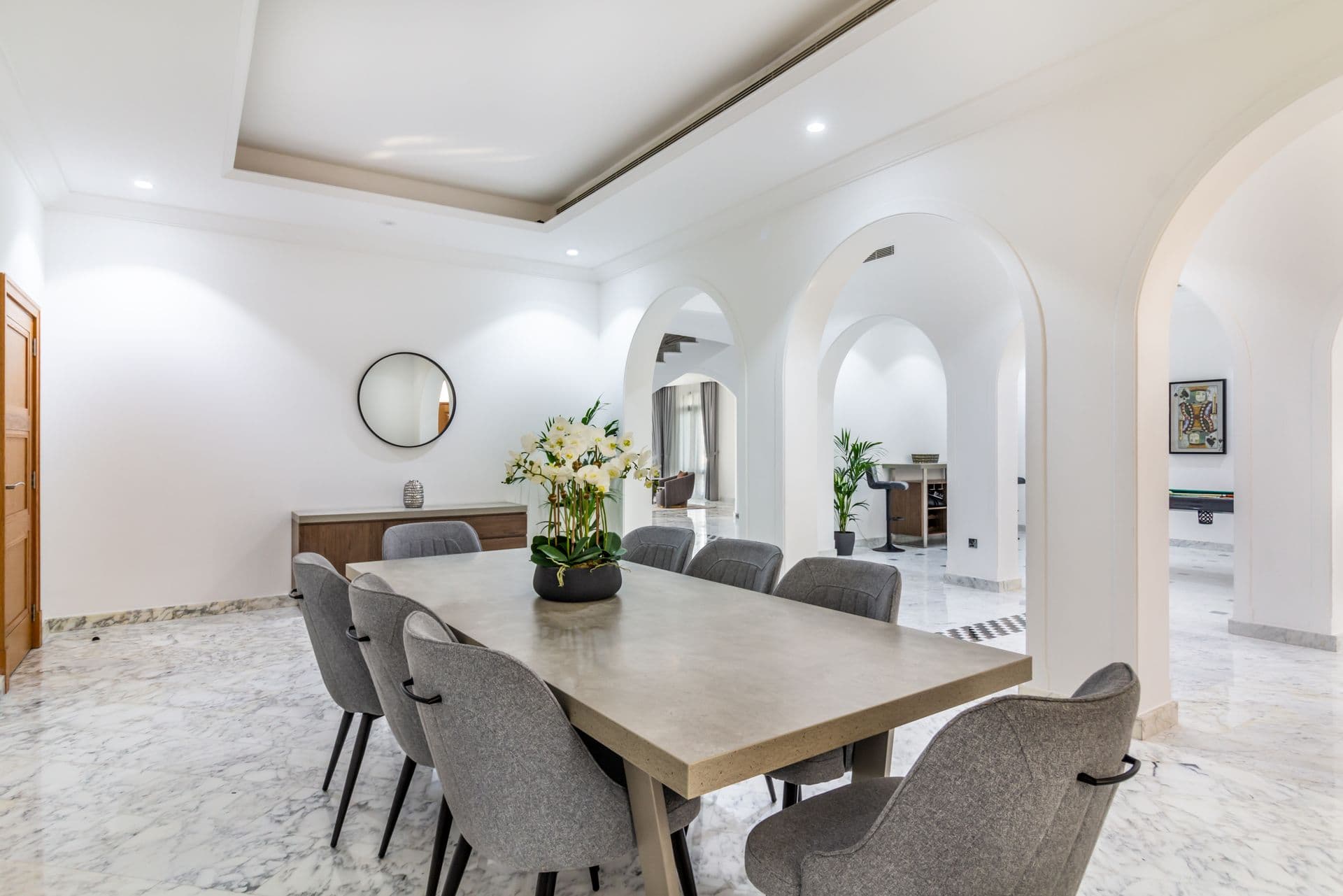 Dining table for eight beneath arched windows on a marble floor