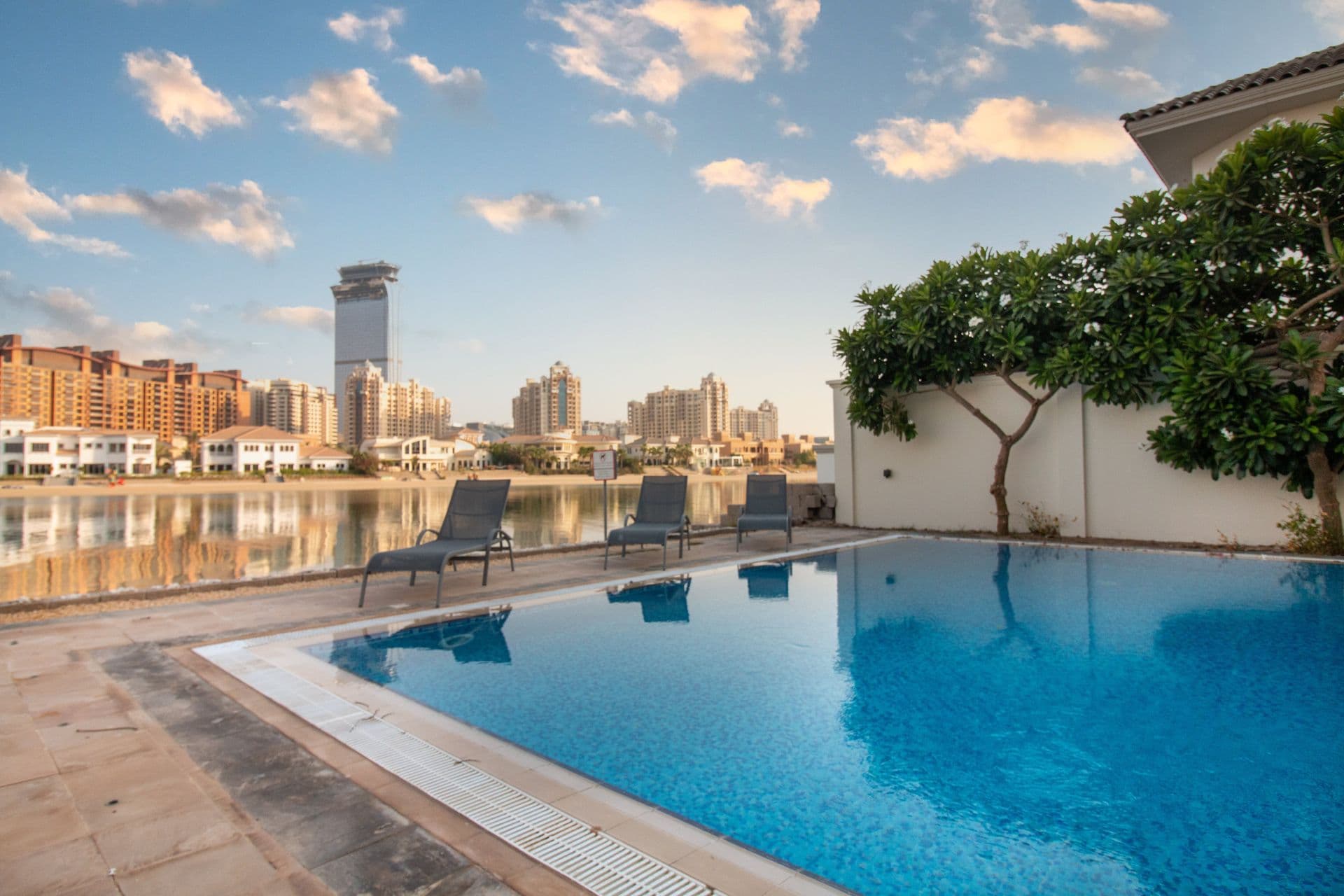 Waterfront villa pool with sun loungers and Dubai skyline at sunset