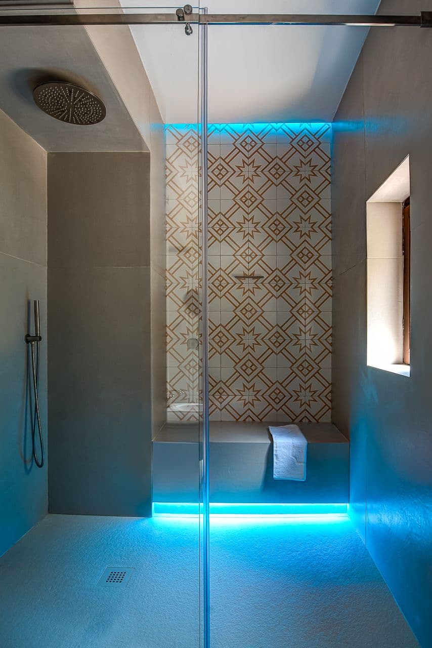 Glass walk in shower with blue mood lighting and patterned tilework at Mount of Love