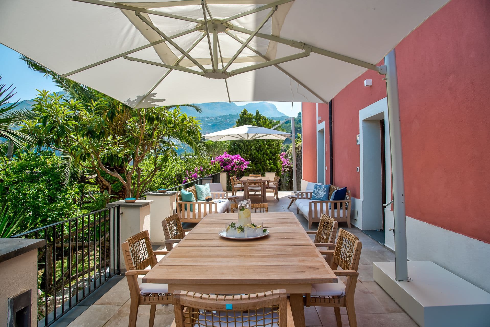 Shaded dining terrace beneath a parasol beside the villa's red facade at Mount of Love