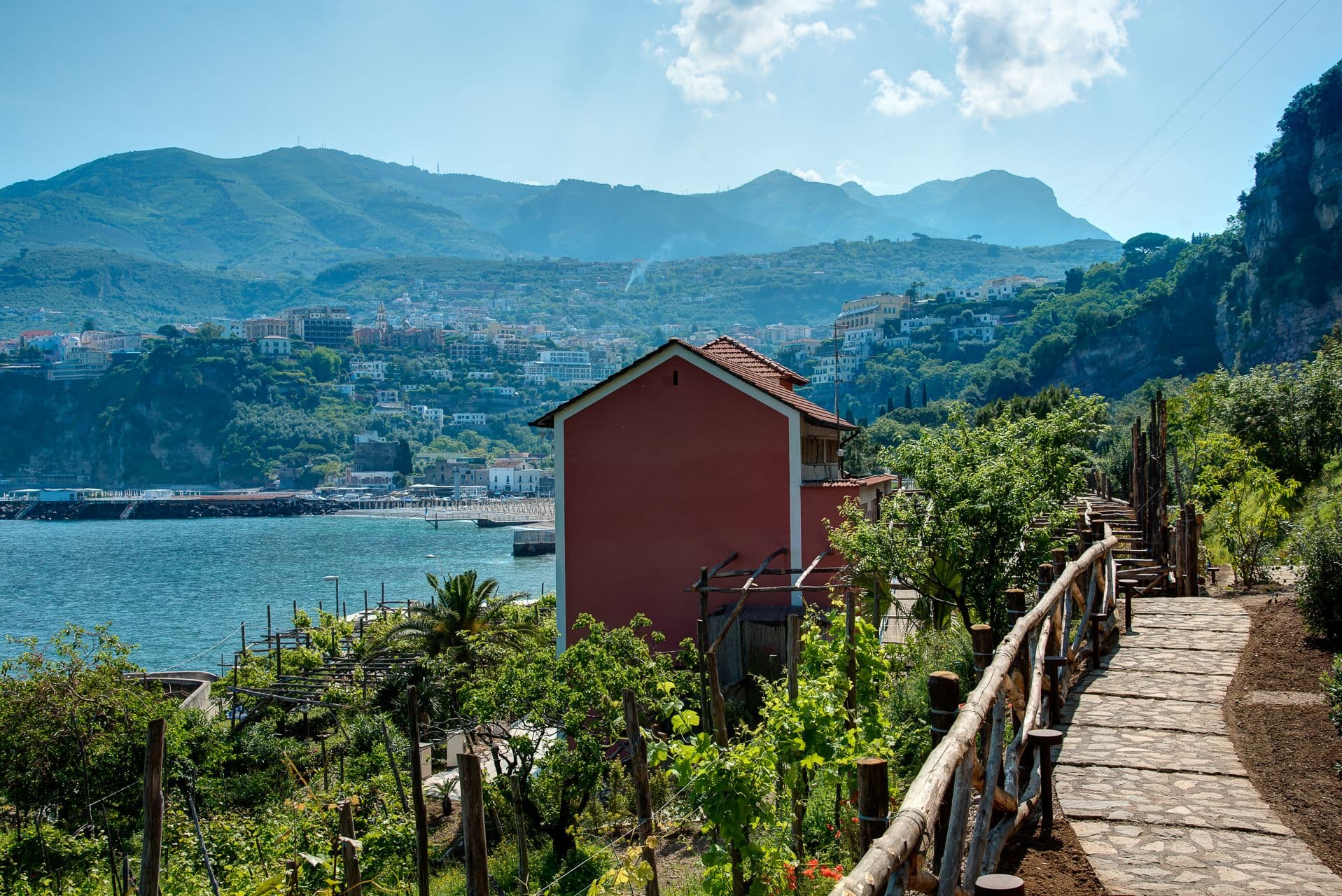 Garden path lined with greenery leading toward a view of the coastal town and sea at Mount of Love