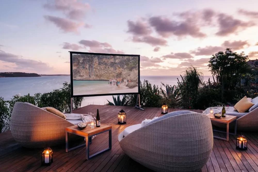 Outdoor cinema deck with woven chairs and lanterns at sunset at Little Bay Villas