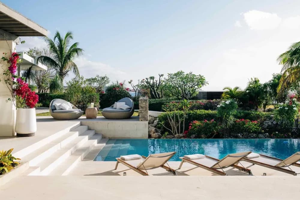 Pool terrace with loungers, woven daybeds and bougainvillea at Little Bay Villas