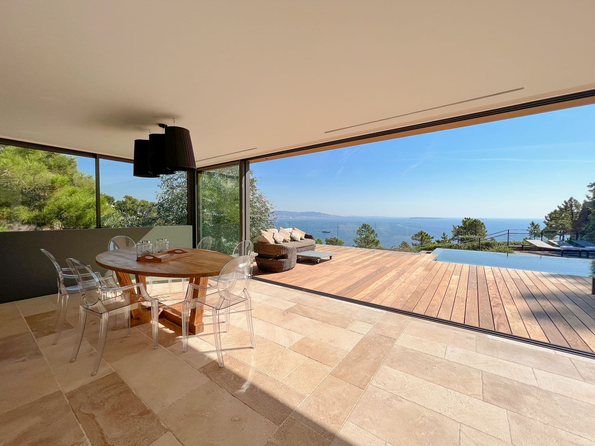 Round timber dining table with ghost chairs opening to the pool terrace at Coastal Azure, Theoule-sur-Mer