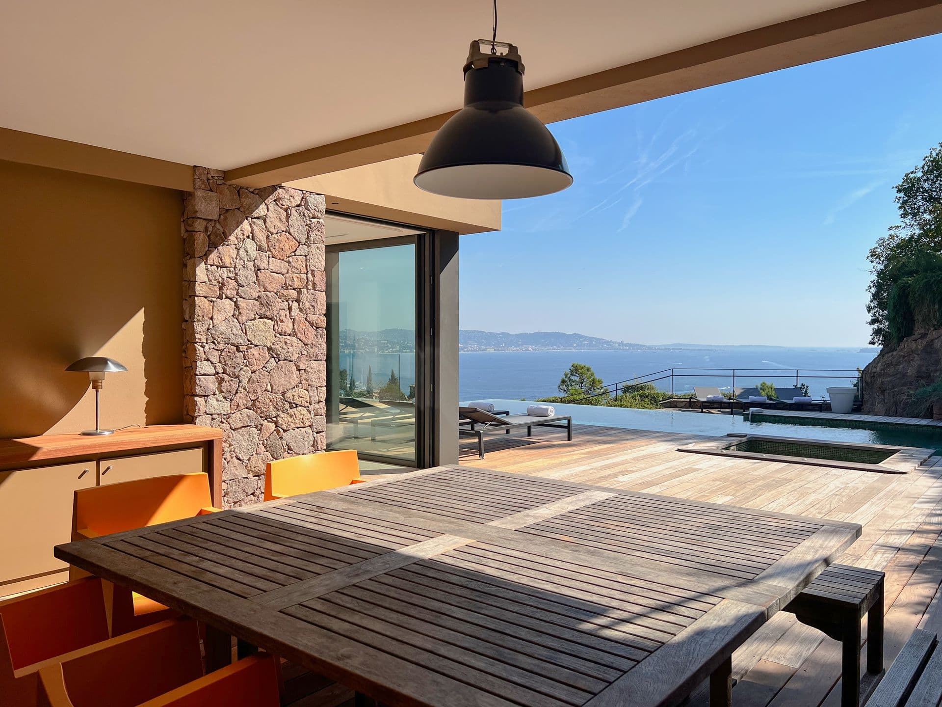 Covered outdoor dining against a stone wall beside the pool and sea at Coastal Azure, Theoule-sur-Mer