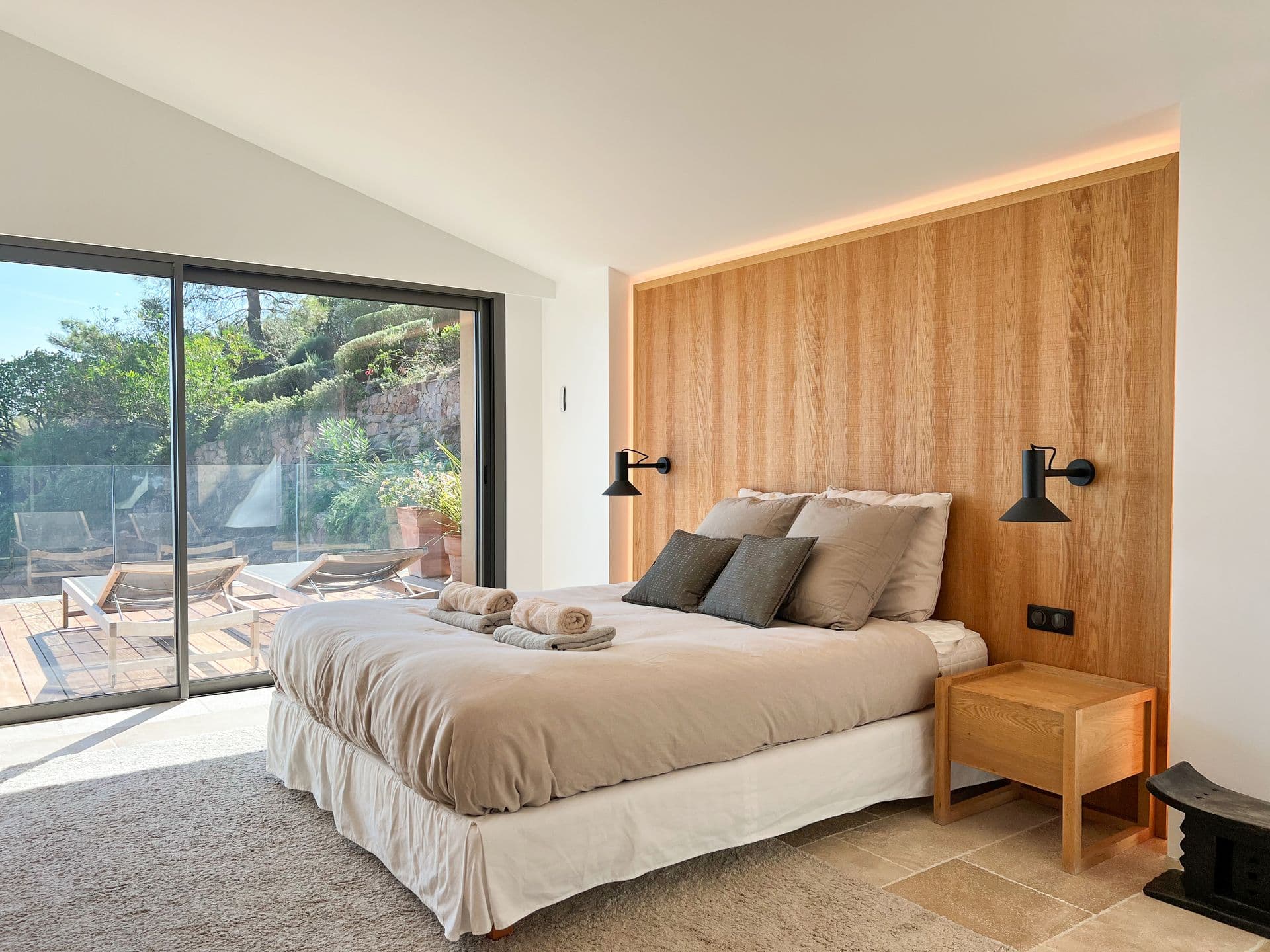 Master bedroom with an oak wall and sliding glass to a sea-view terrace at Coastal Azure, Theoule-sur-Mer