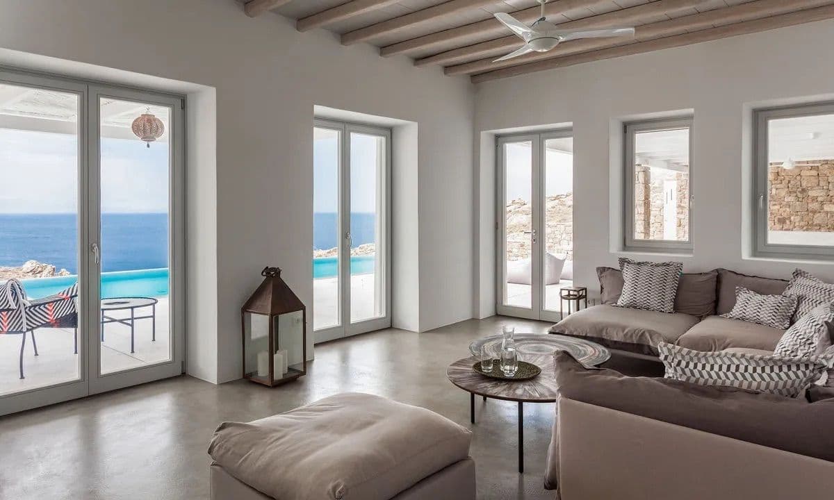 Living room with grey sofas opening through glazed doors to the sea at Ancient Azure Vistas, Mykonos