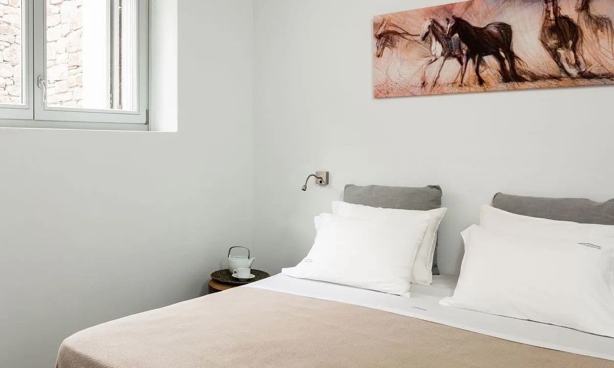 Master bedroom with a grey upholstered headboard and equine artwork at Ancient Azure Vistas, Mykonos