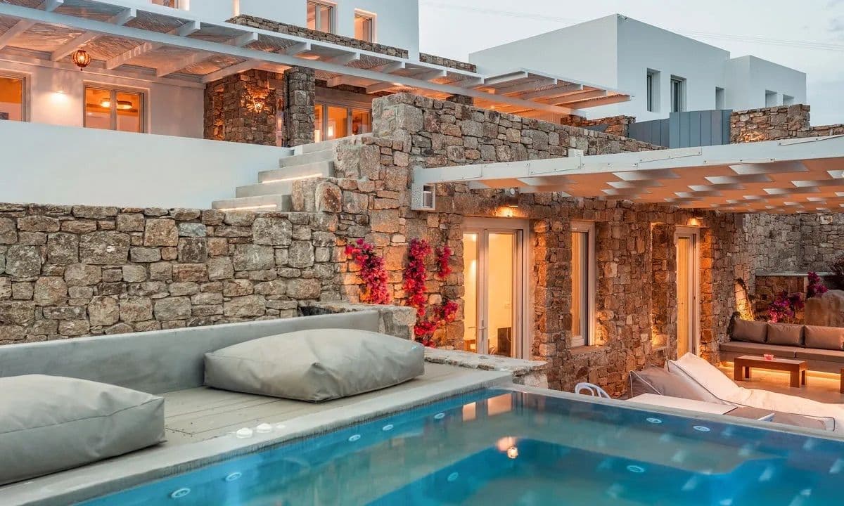 Stone villa and lit pool at dusk with loungers at Ancient Azure Vistas, Mykonos