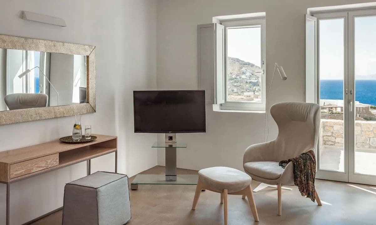 Bedroom suite with a reading chair, television and sea-view doors at Ancient Azure Vistas, Mykonos