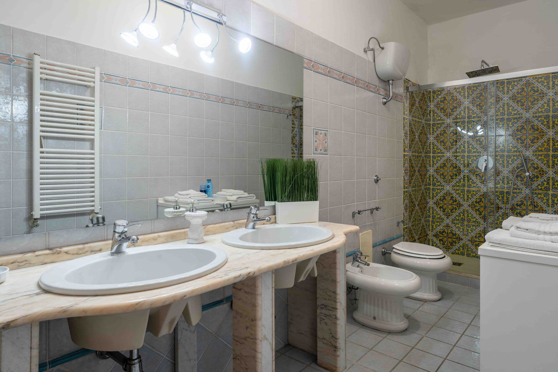A bathroom with a double sink vanity, mirror and patterned floor tiles