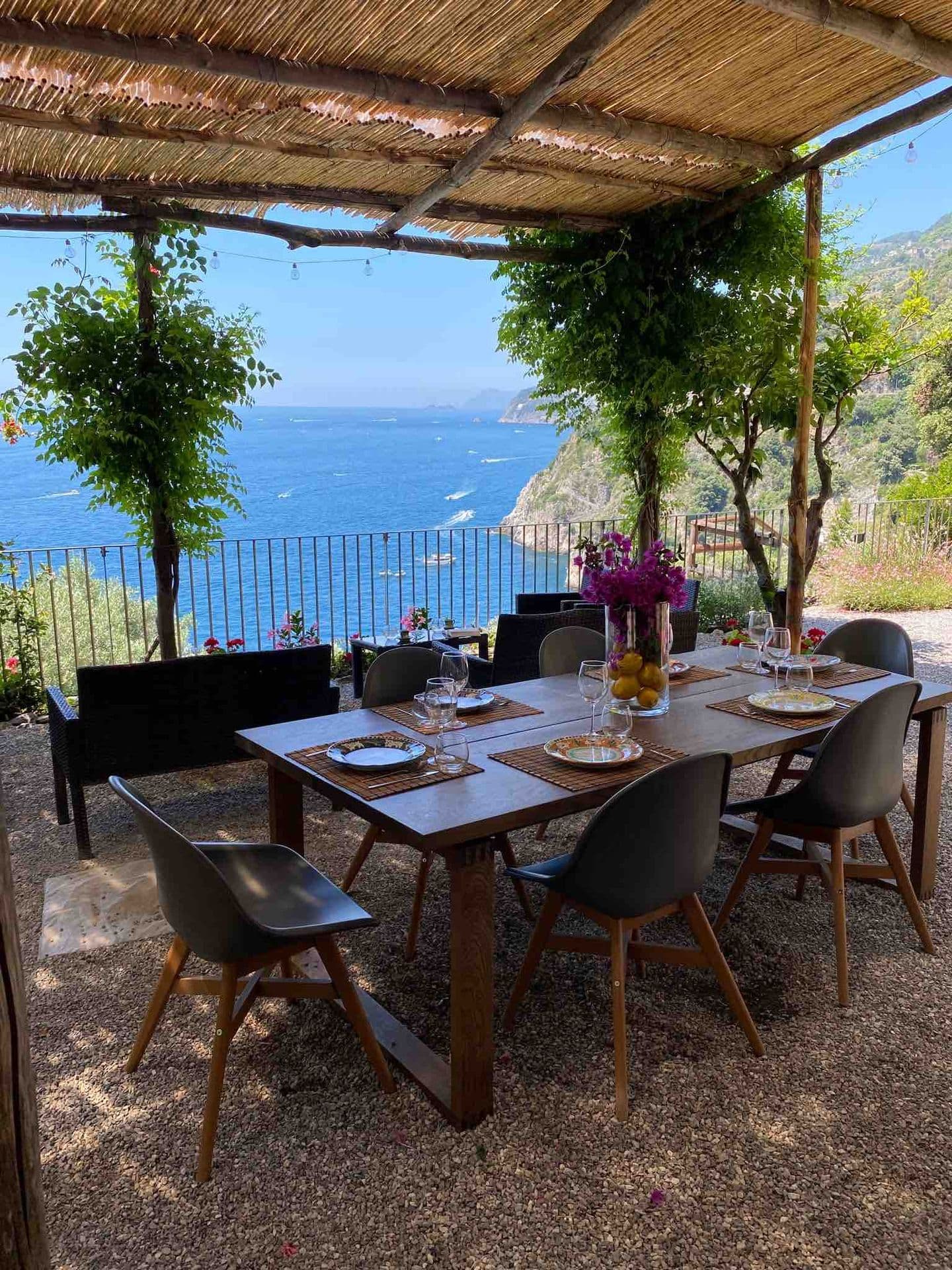 An outdoor dining table under a reed pergola with sea views