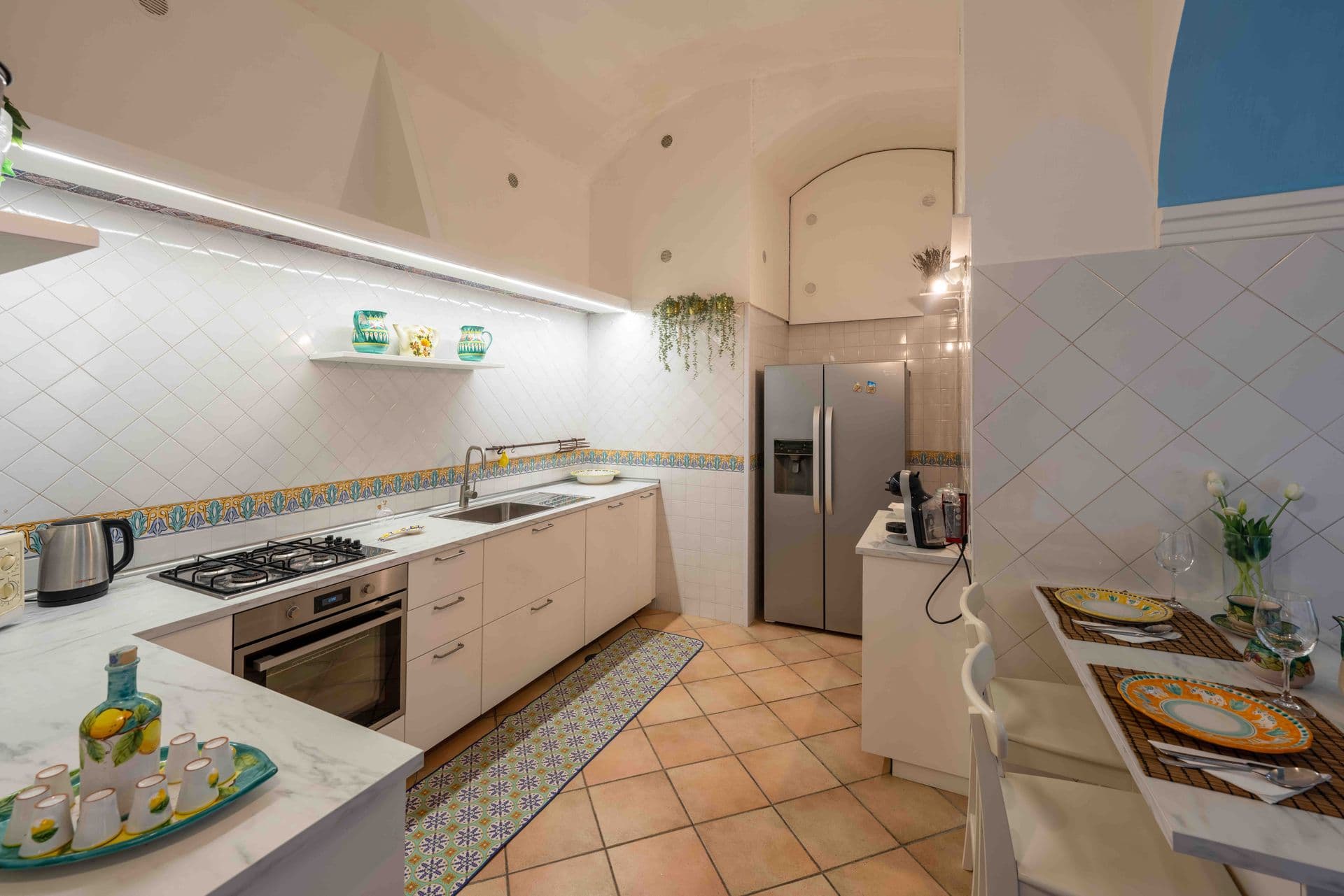 A white tiled kitchen with patterned splashback and a small dining nook
