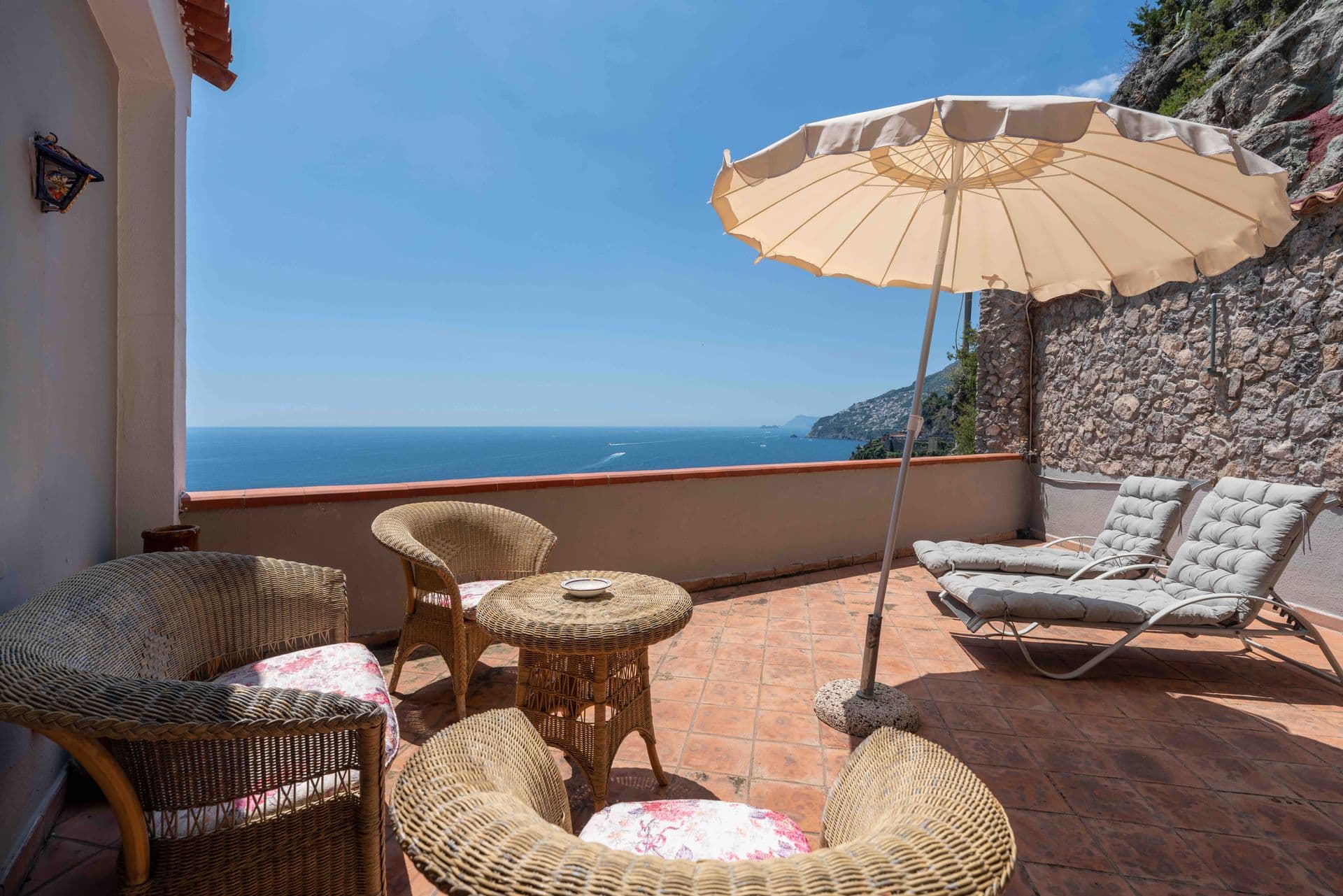 Wicker armchairs and a parasol on a terrace with uninterrupted sea views