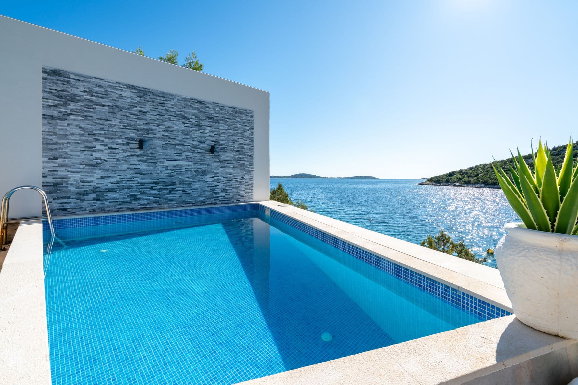 Poolside terrace above a rocky cove with the villa and coast behind at Blue All Around, Marina, Croatia