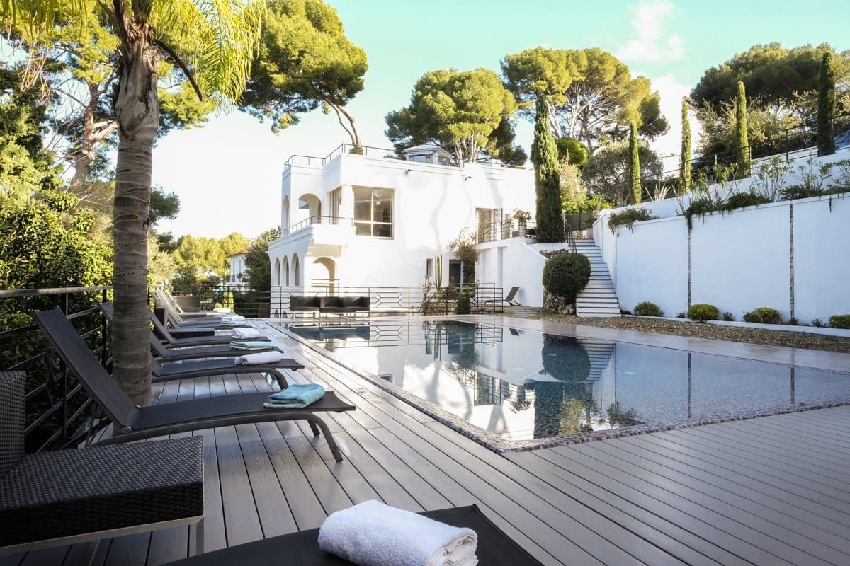 Wooden pool deck with dark loungers and palm trees beside the villa