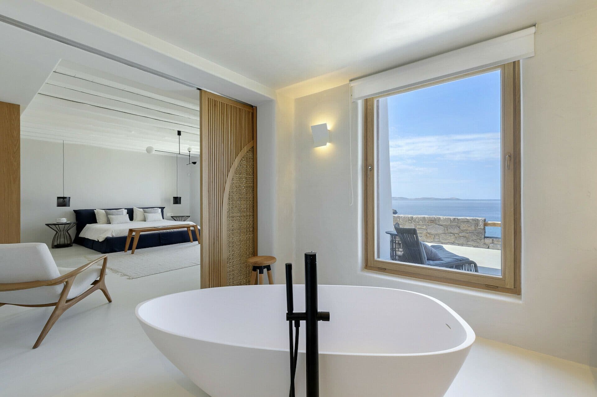Bedroom suite with a freestanding tub beside a sea-view window at Cycladic Wonder, Mykonos