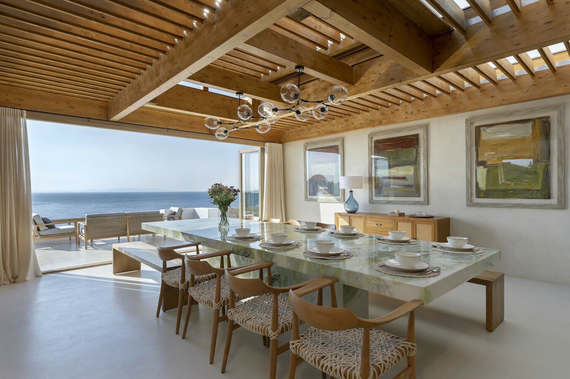 Glass dining table beneath a timber pergola with sea views at Cycladic Wonder, Mykonos
