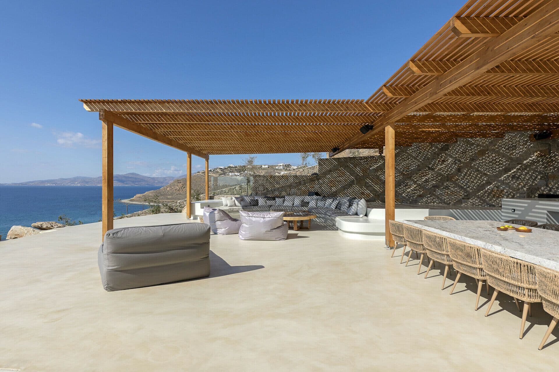 Pergola-shaded outdoor dining and lounge terrace above the sea at Cycladic Wonder, Mykonos