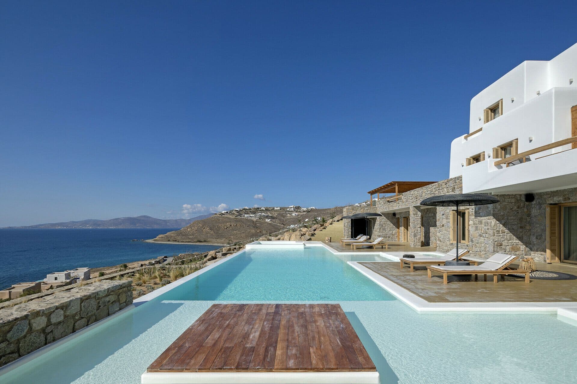 Infinity pool and timber deck beside the white villa overlooking the sea at Cycladic Wonder, Mykonos