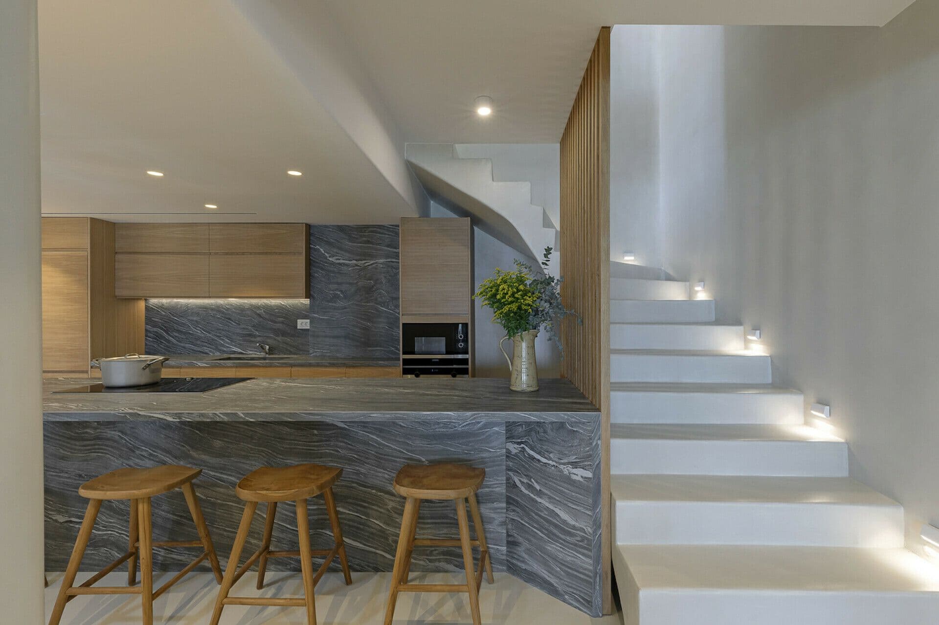 Kitchen with a grey-marble island and bar stools beside the staircase at Cycladic Wonder, Mykonos