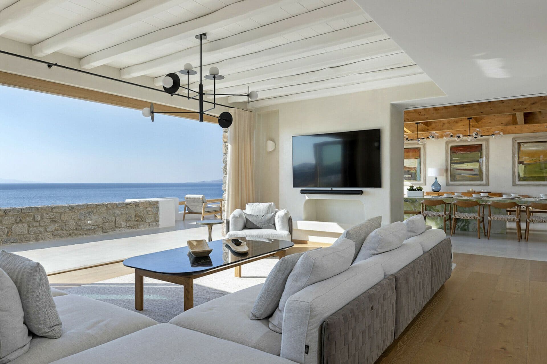 Living room with a grey sofa and television opening to the sea at Cycladic Wonder, Mykonos