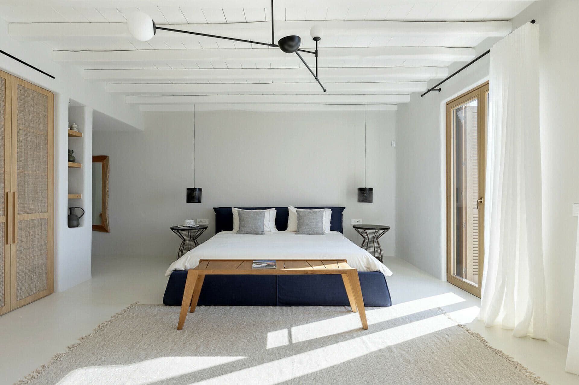 Master bedroom in white with a navy bench and sheer curtains at Cycladic Wonder, Mykonos