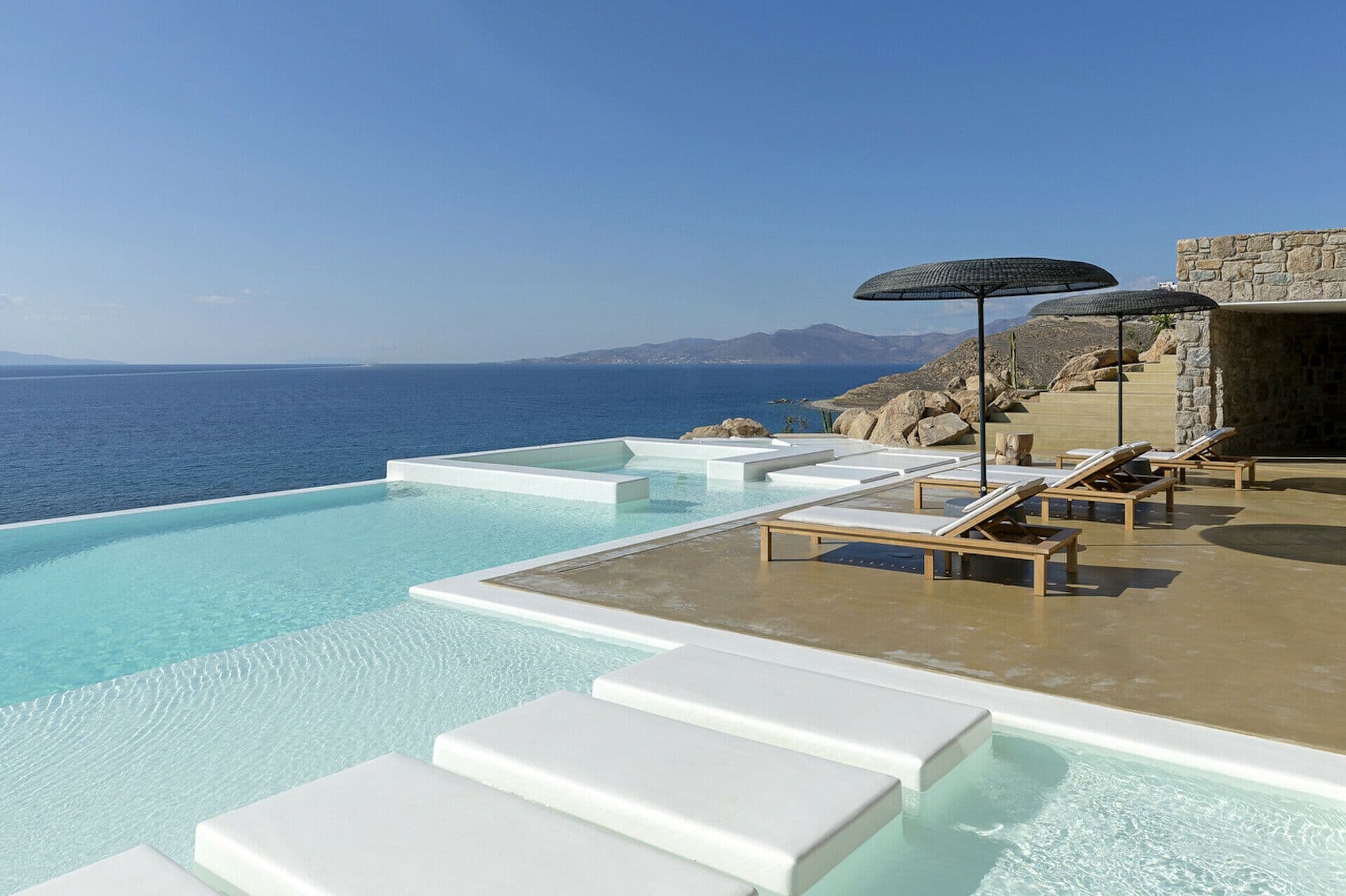 Infinity pool with loungers on a stone terrace above the sea at Cycladic Wonder, Mykonos