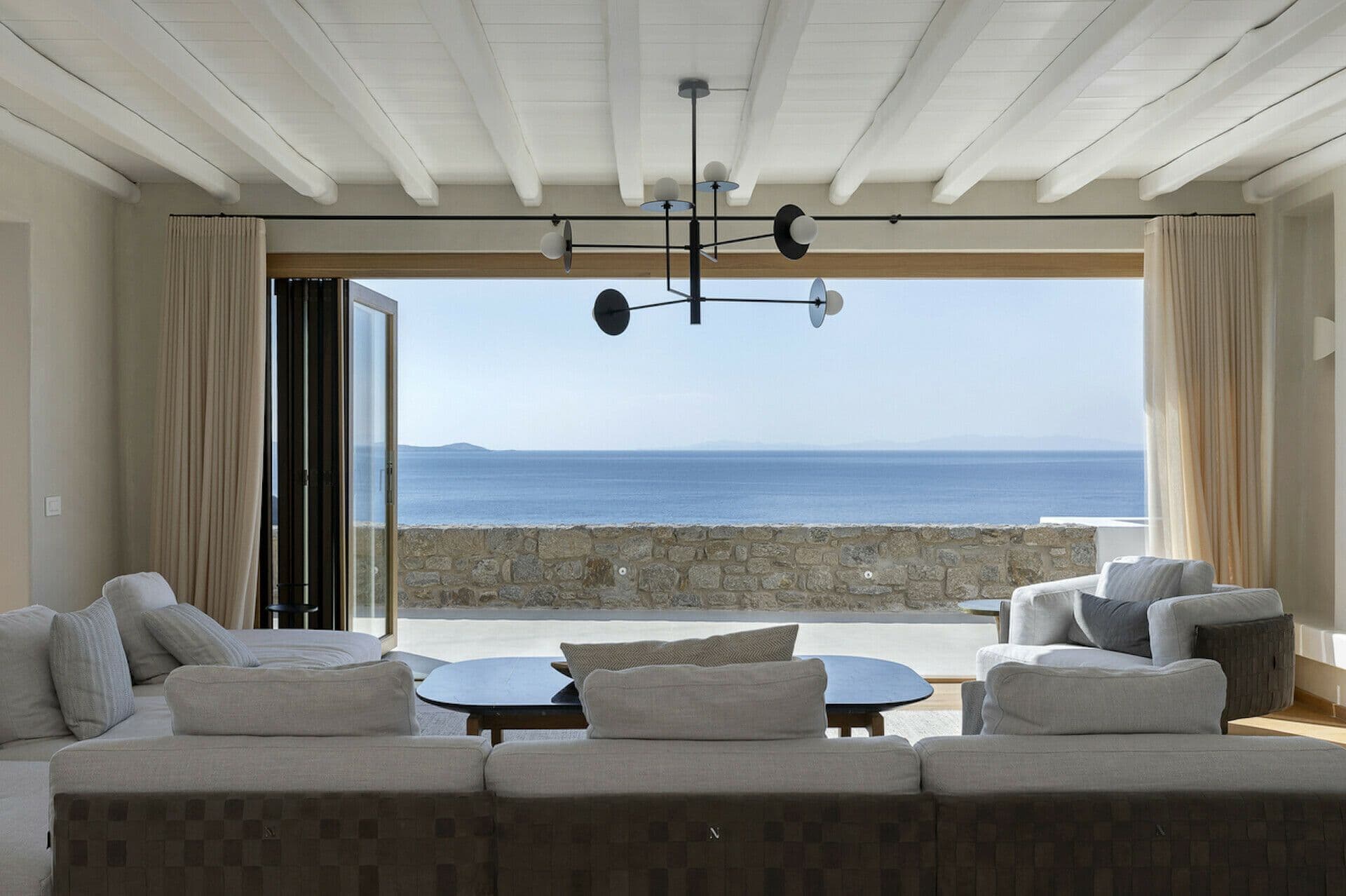 Sitting area with sage sofas and a round table beside a sea-view window at Cycladic Wonder, Mykonos