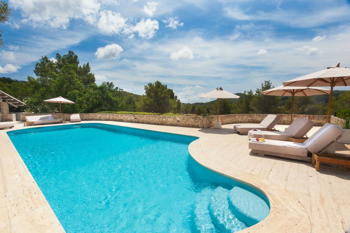 Curved swimming pool with sun loungers and pine-covered hills beyond