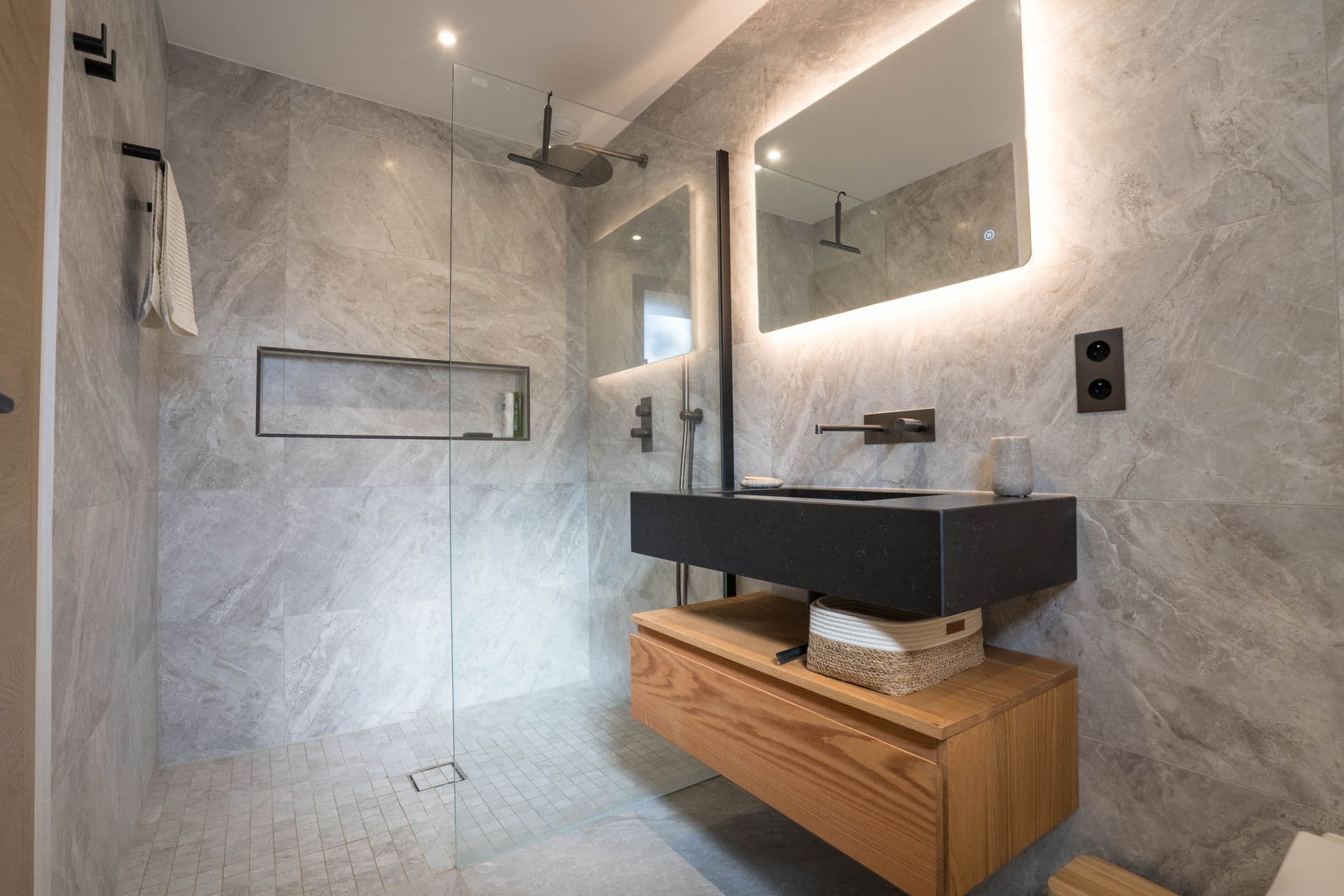 Stone-tiled bathroom with a walk-in shower and backlit vanity mirror